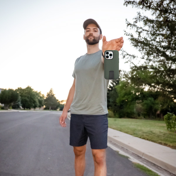 A man is holding out his hand after dropping his phone with a Green motus phone case on it.