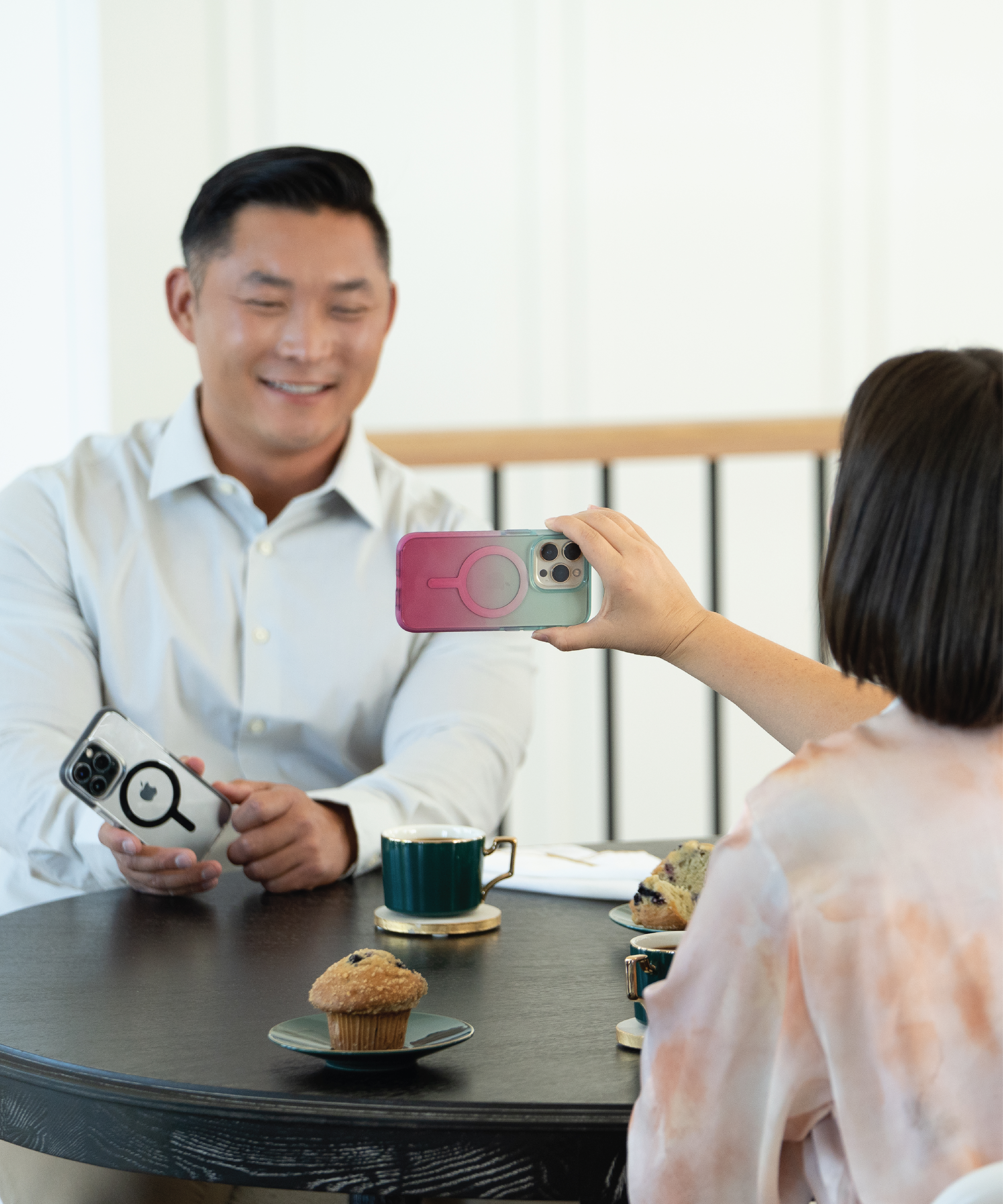 A woman is holding her phone out to a man to show him something on her screen. The woman's phone has an ombre ace pro magsafe case on it and the mans phone has a clear/black ace pro magsafe case on it.