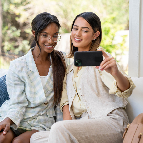 Two women are sitting next to each other taking a selfie. Their phone has a black motus phone case on