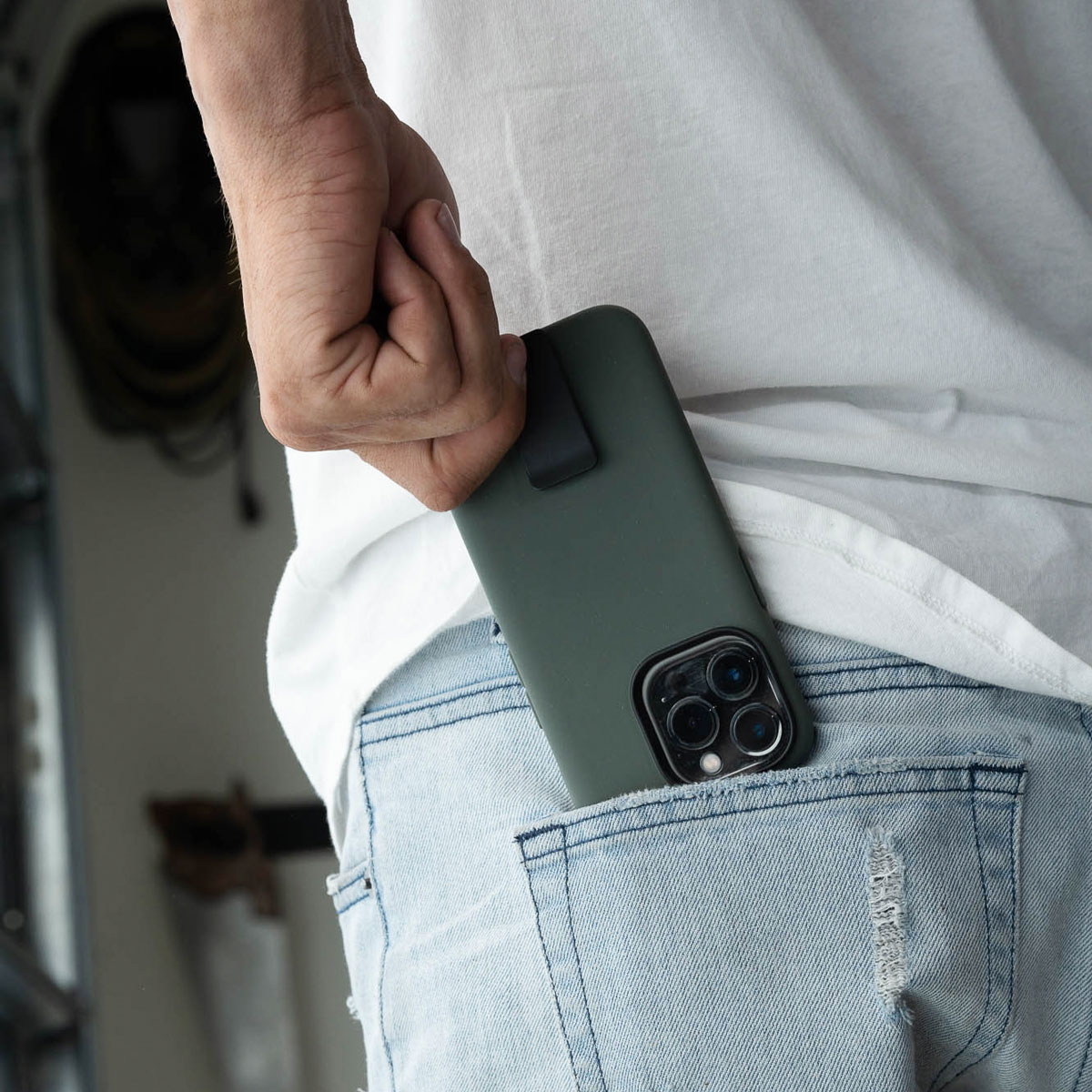 Person tucking their phone with a green Motus phone case into their back pocket.