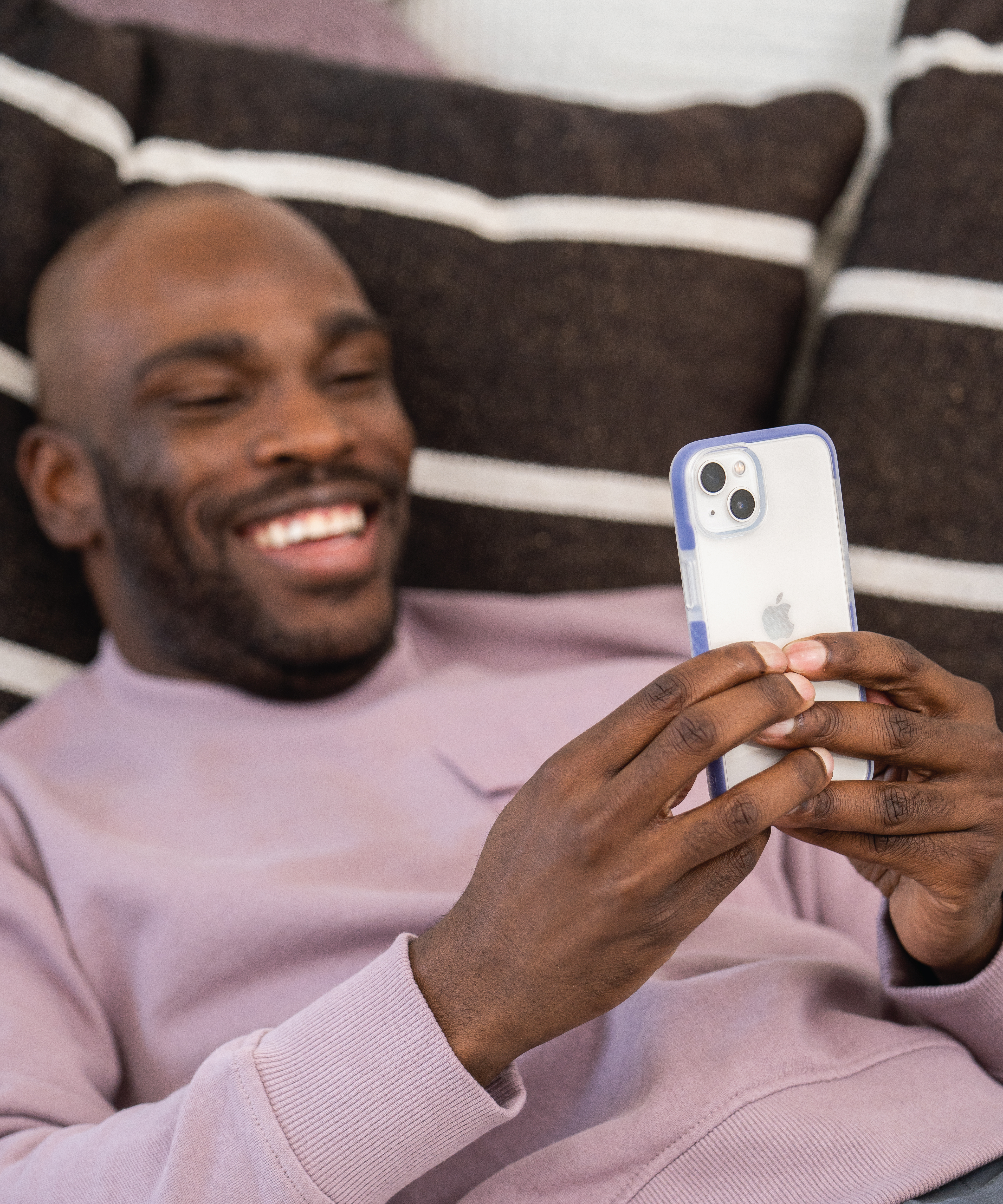 Man laying on couch using an iphone 14 with a blue ace pro case on it.